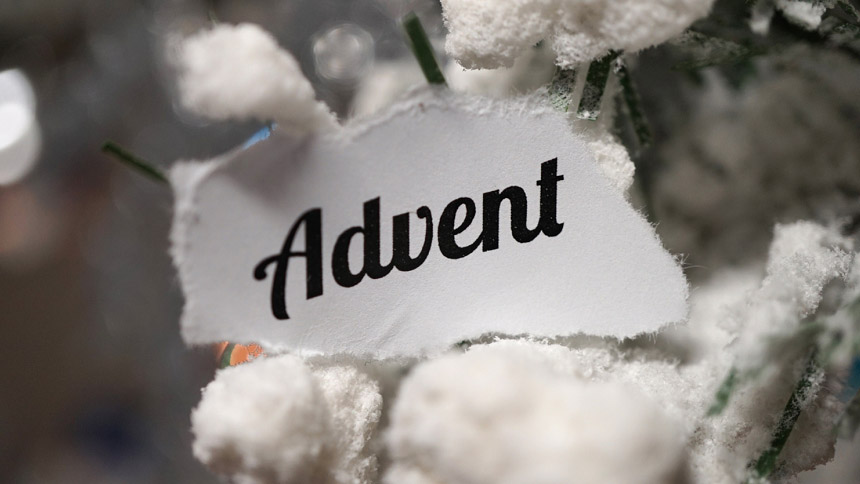 piece of white paper with "Advent" printed on it resting on snow-covered branches