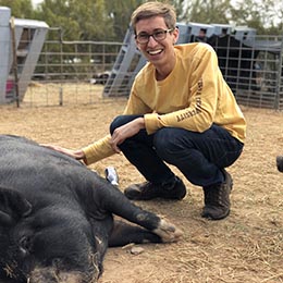 Eric Arellano kneeling next to large black pig