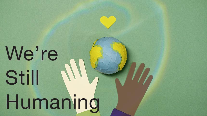 "We're Still Humaning" text over a paper collage of the earth with a yellow heart above it, cradled by two hands: 1 tan, 1 brown