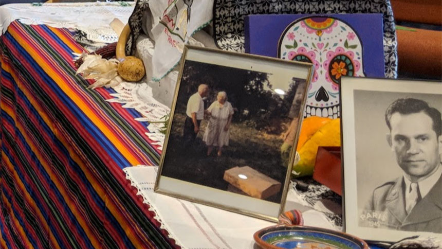 A Dia de los Muertos altar containing personal photos, a picture of a skull and other decorations.