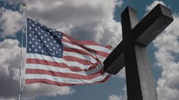 A picture of an American flag next to a cross with blue skies in the background