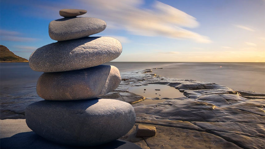 Photo of stack of stones on a flat beach, light blue sky with wispy clouds