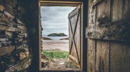 A picture of an open door looking out on to a beach with water and an island in the background.